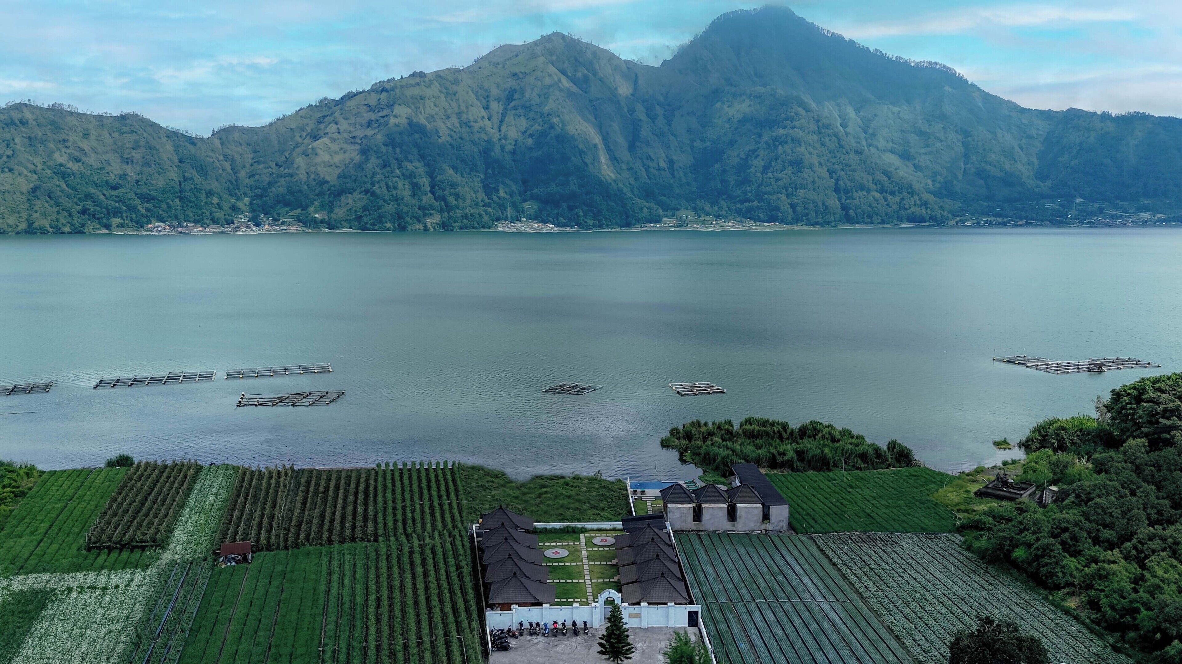 A lakeside property with terraced gardens, a central building with a traditional roof, and a mountainous backdrop.