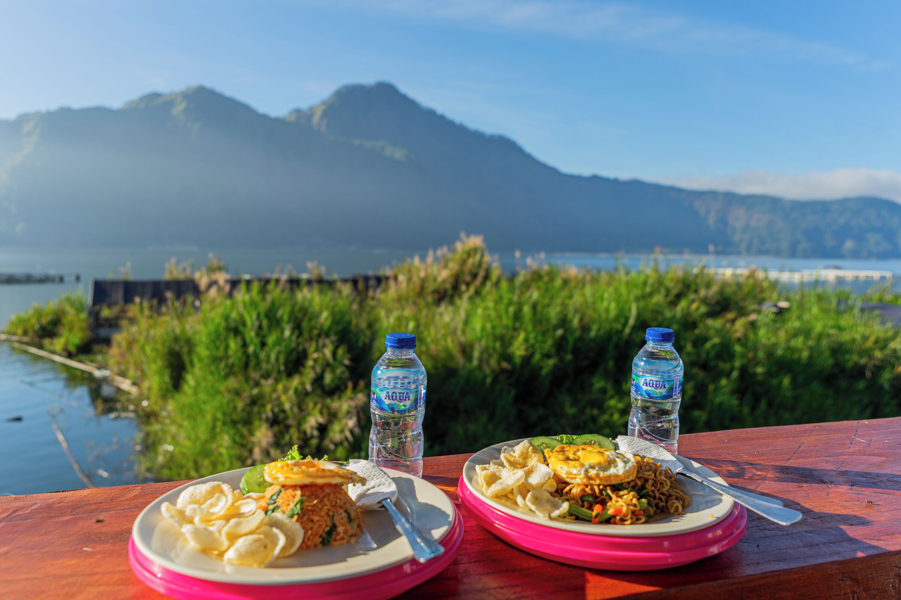 Zwei Teller Essen auf einem Holztisch, im Hintergrund ein Gewässer und Berge.