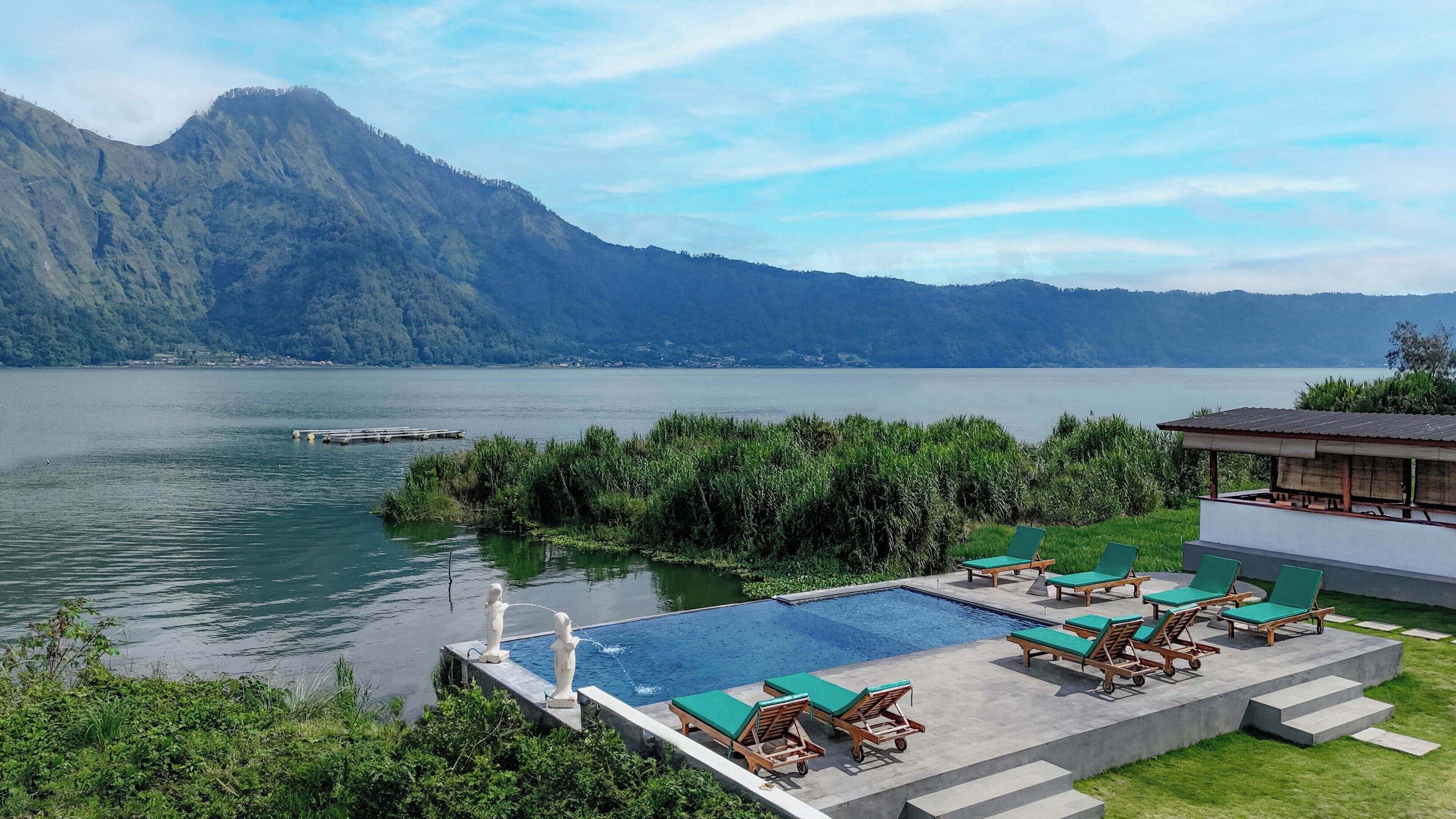 A pool area with lounge chairs and a view of a lake and mountains.