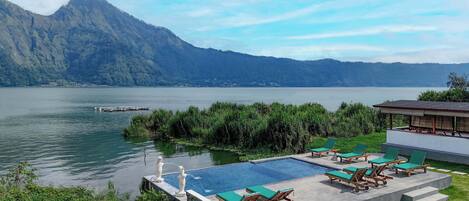 A pool area with lounge chairs and a view of a lake and mountains.