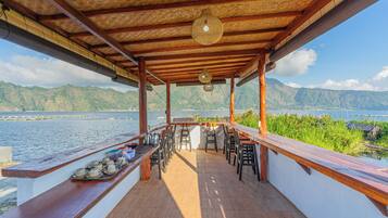 A covered outdoor seating area with a view of a lake and mountains.