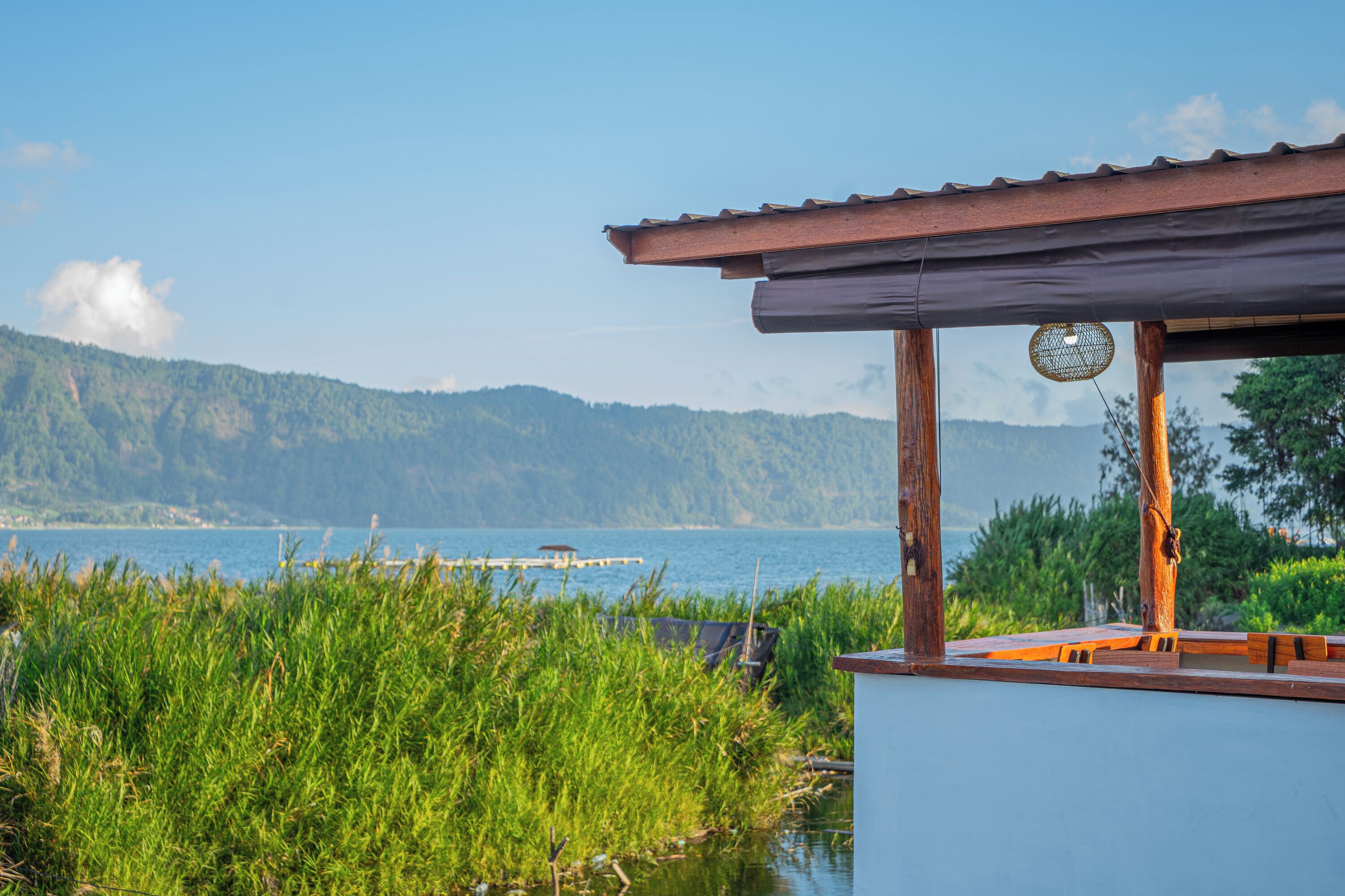 A wooden structure with a metal roof overlooking a body of water and a distant shoreline.