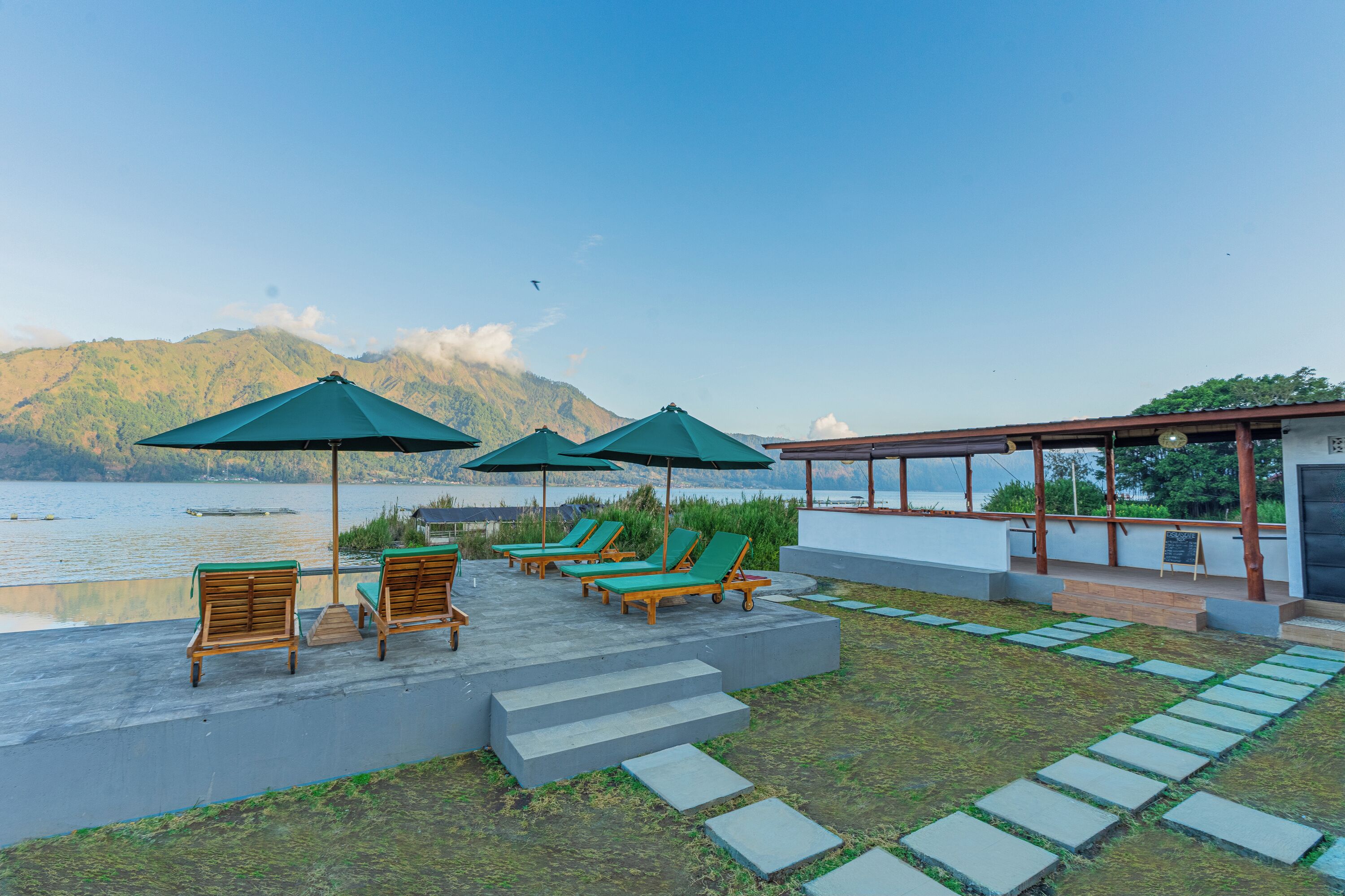 Une terrasse dotée de chaises longues et de parasols, offrant une vue sur un lac, avec des montagnes en arrière-plan.