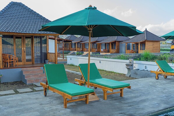 Ein Resort mit Holzhütten, grünen Liegestühlen und einem Poolbereich.