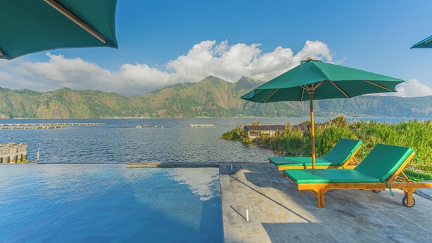 A poolside area with lounge chairs and umbrellas overlooking a body of water and mountains. - D Sila’s Tepi Danu Villas Kintamani & Natural hot spring (Kintamani)