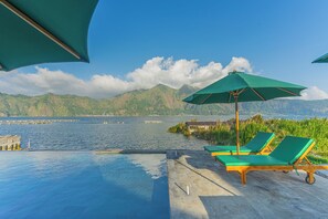 Ein Poolbereich mit Liegestühlen und Sonnenschirmen mit Blick auf ein Gewässer und Berge.
