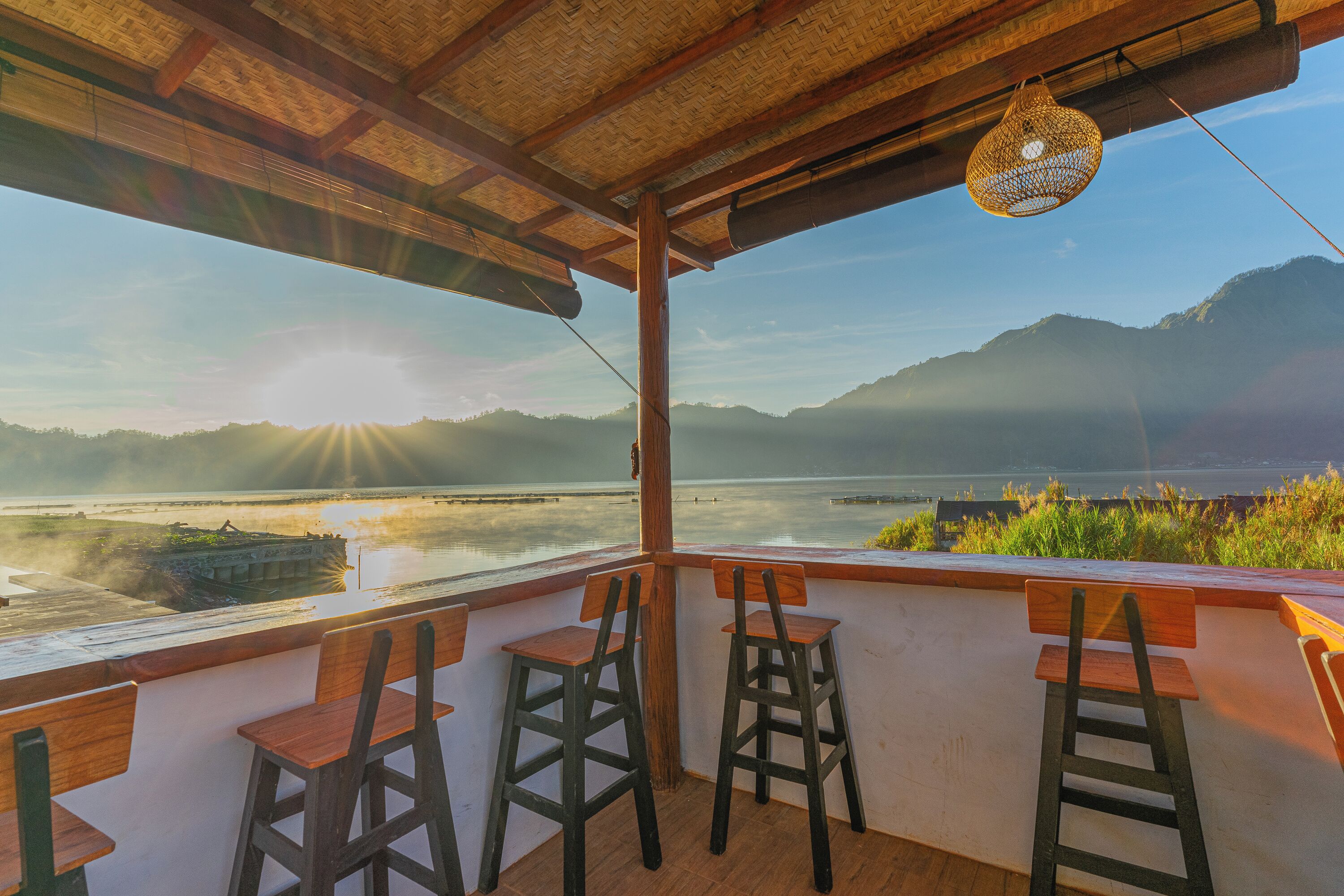 A terrace with wooden chairs and a ladder, overlooking a body of water and mountains.