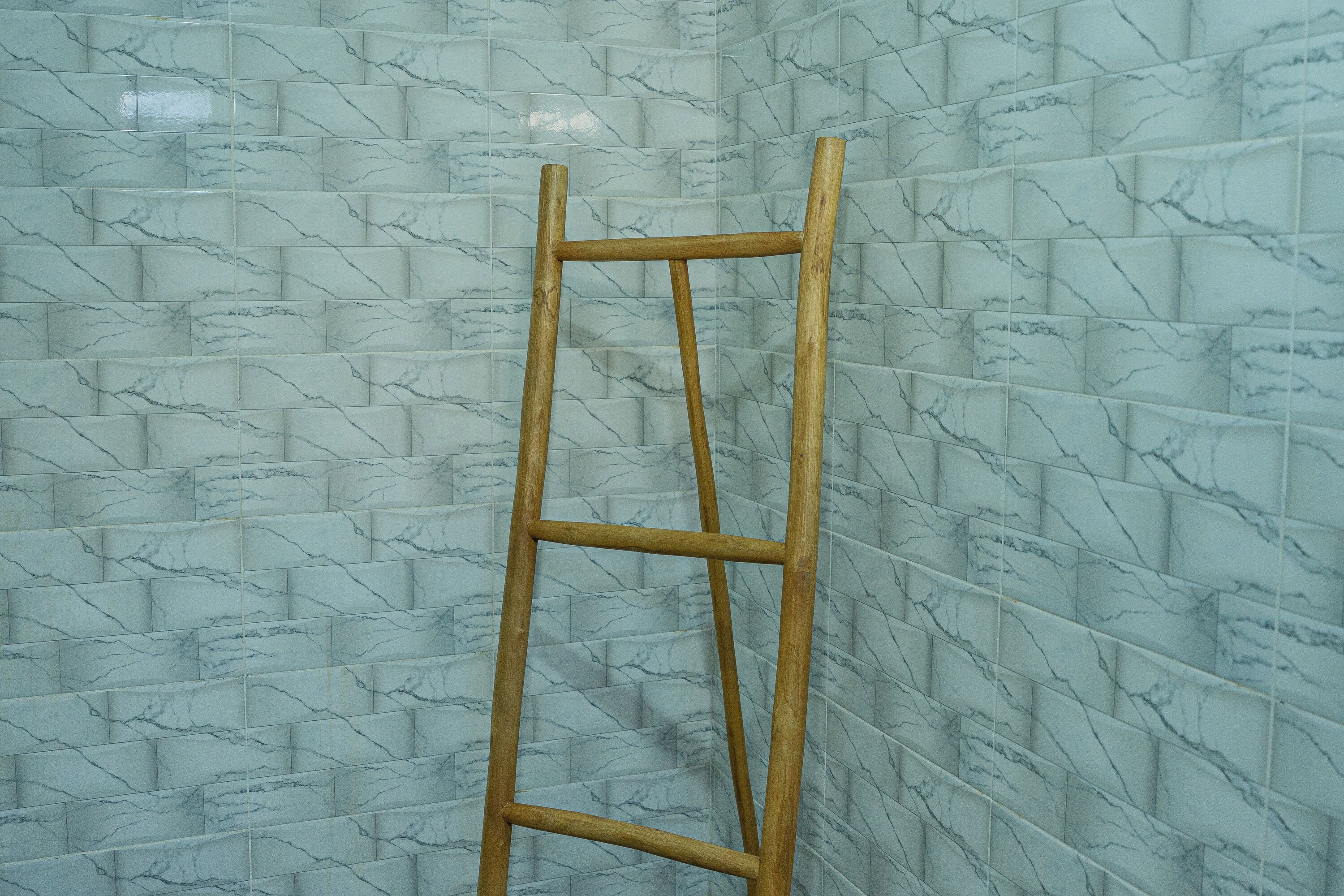 Una escalera de madera apoyada en una pared con baldosas de diseño de mármol.