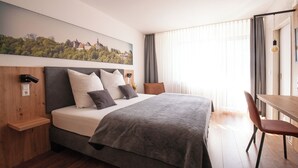 A modern hotel room with a large bed, a wooden nightstand, a desk, and a chair. - Hotel Garni Zum Wilden Mann (Künzelsau)