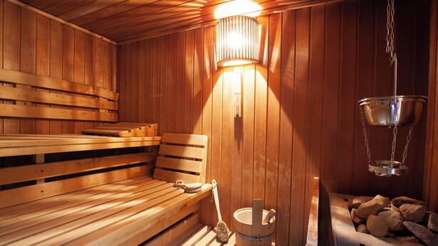 A wooden sauna with benches, a wooden bucket, and a hanging metal container. - Hotel Garni Zum Wilden Mann (Künzelsau)