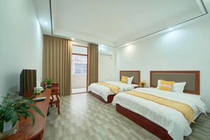 Une chambre d’hôtel avec deux lits, un bureau avec une chaise, une télévision et une fenêtre avec des rideaux.