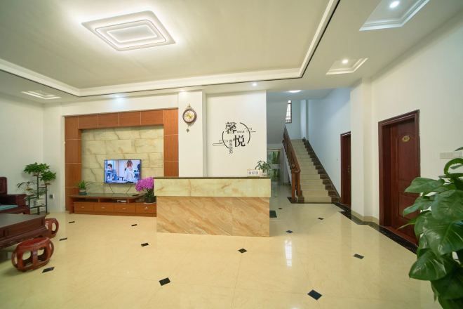 A hotel lobby with a reception desk, a TV, a staircase, and a plant.