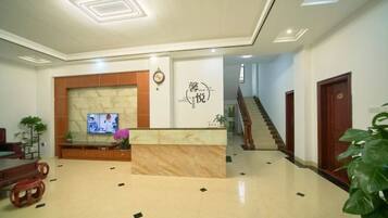 A hotel lobby with a reception desk, a TV, a staircase, and a plant.