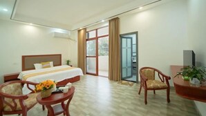 A hotel room with a bed, a desk, a chair, a small table with a vase of flowers, and a sliding glass door leading to an outdoor area. - Mount Danxia Xin Yue Inn (Renhua)