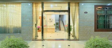 A hotel entrance with a glass door, a reception desk, and a staircase leading to the upper floor.