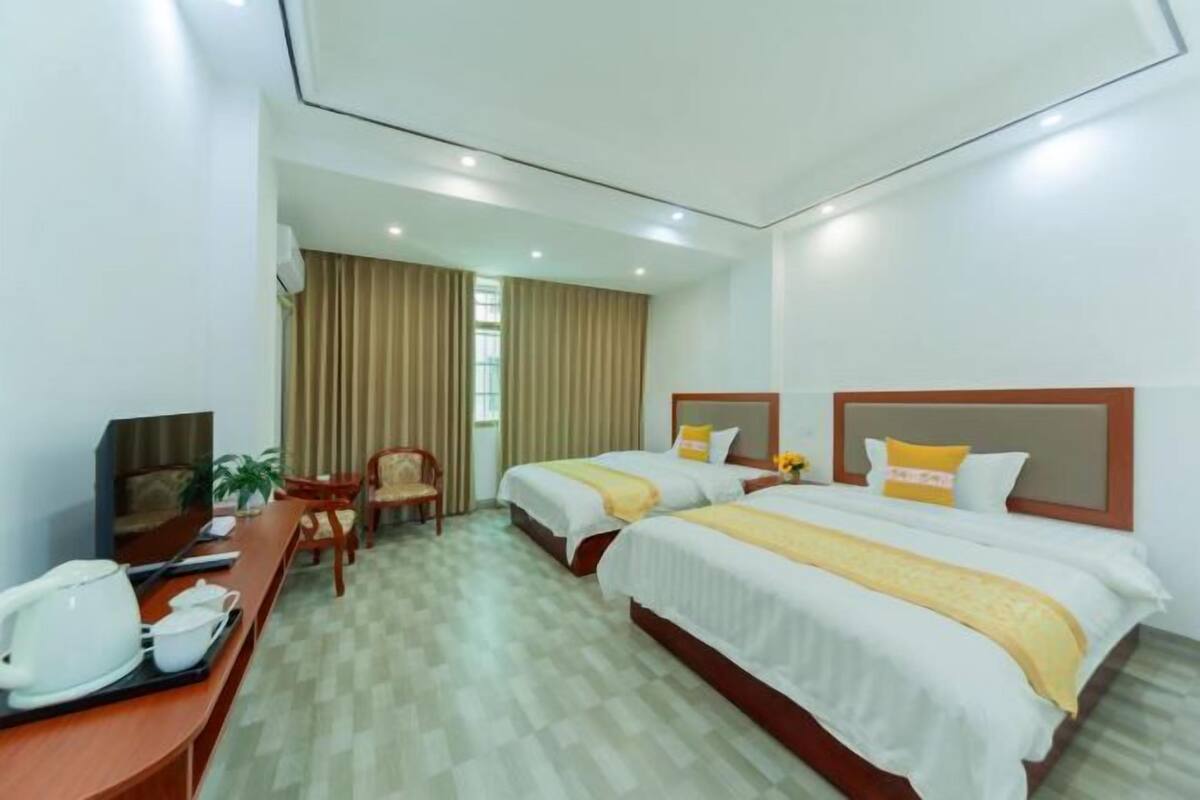 A hotel room with two beds, a desk with a coffee maker, a chair, and a window with curtains.