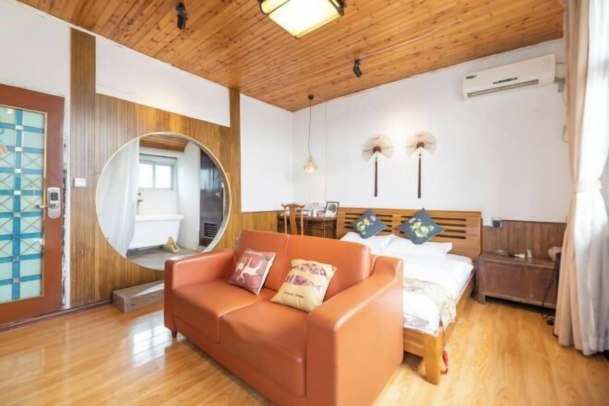 A room with a wooden ceiling, a round mirror, a bed with two pillows, a wooden nightstand, and a small table.