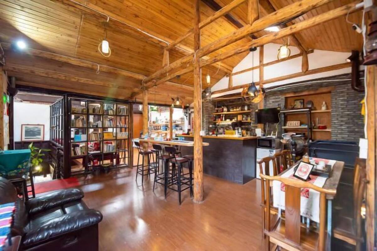 A spacious room with a wooden ceiling, a bar area with stools, a bookshelf, and a seating area with a leather couch.