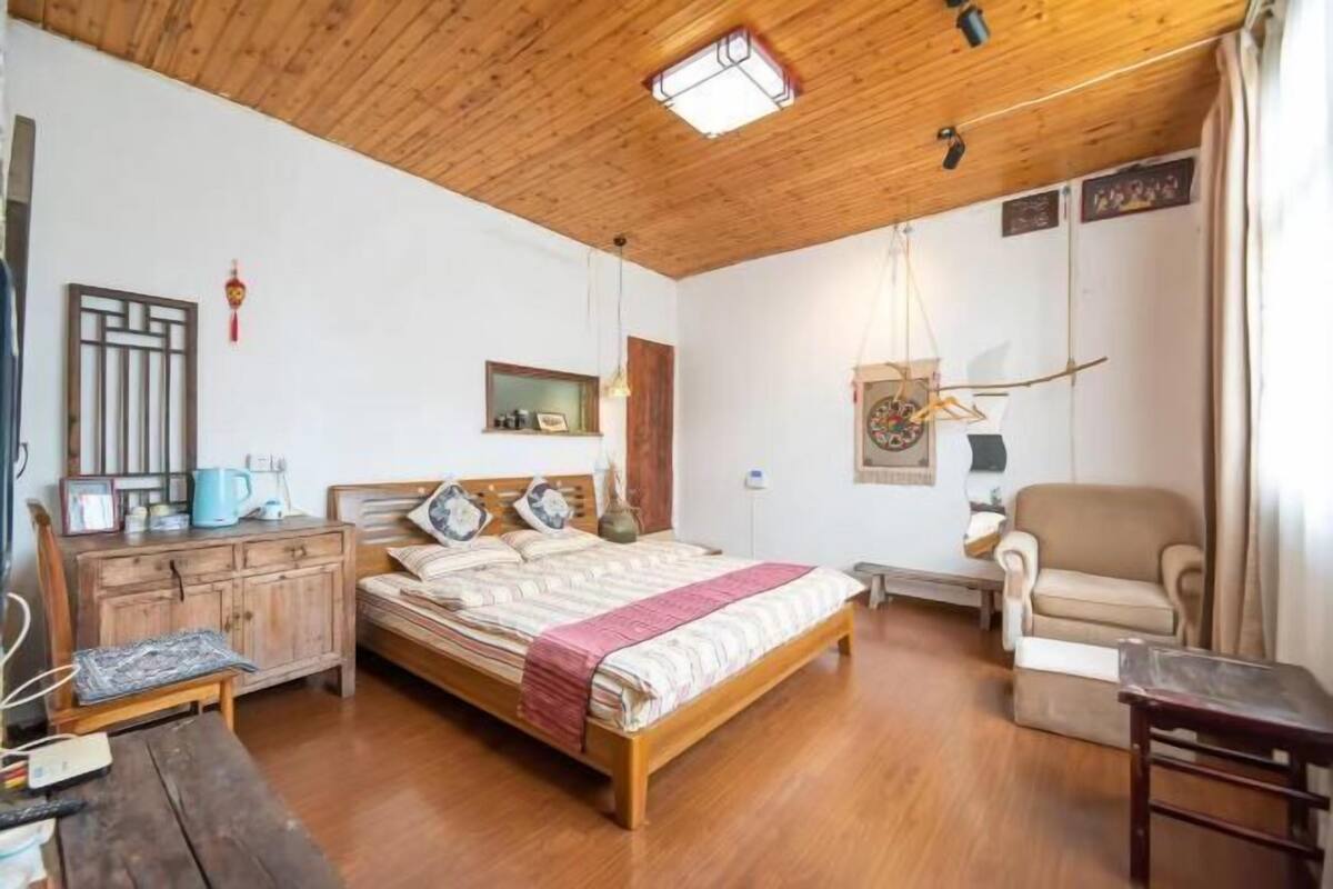 A wooden ceiling, a bed with pillows, a chair, a small table, and a cabinet.