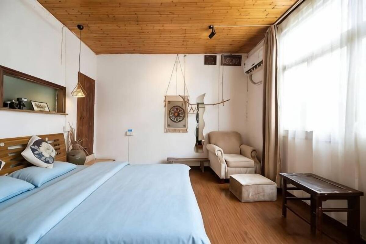 A bedroom with a bed, a chair, a small table, and a window with curtains.