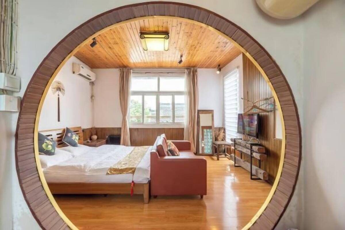 A circular room with a bed, a red sofa, a TV, and a window.