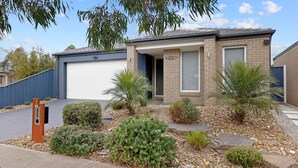 A modern two-story house with a garage, a well-maintained garden with various shrubs and a palm tree, and a clear blue sky. - Life's a Beach Shack (Cowes)