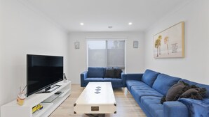 A modern living room with a flat-screen TV, a blue sofa, and a coffee table. - Life's a Beach Shack (Cowes)