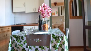 A kitchen with white cabinets, a table with a green leaf-patterned tablecloth, a chair, and a vase with pink flowers. - Holiday home with balcony and air conditioning in Torre dell'O (Torre dell'Orso)