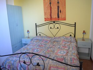 Een slaapkamer met een bedovertrek met dessin, een hoofdbord in de vorm van een hart, twee nachtkastjes met lampen en een kledingkast.