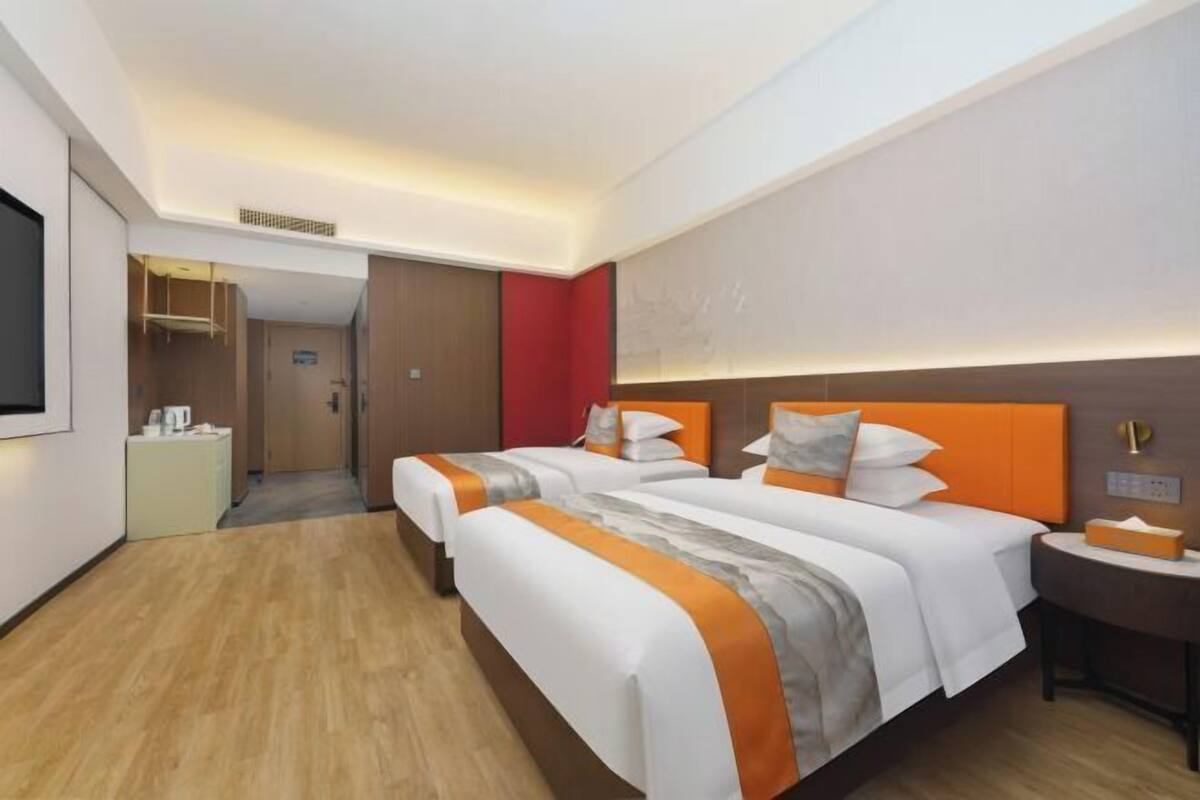 Ein Hotelzimmer mit zwei Betten, einem Nachttisch, einem Fernseher und einer Tür zu einem Flur.