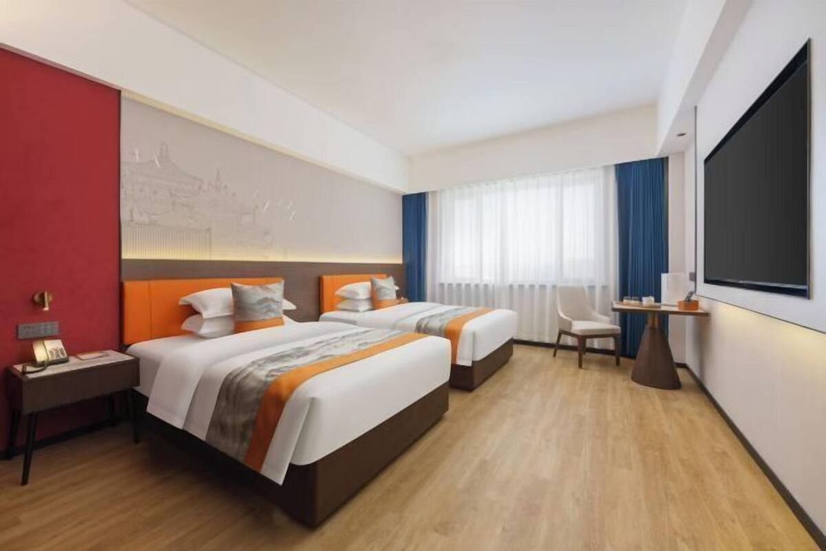 Ein Hotelzimmer mit zwei Betten, einem Schreibtisch, einem Stuhl, einem Fernseher und einem Fenster mit Vorhängen.