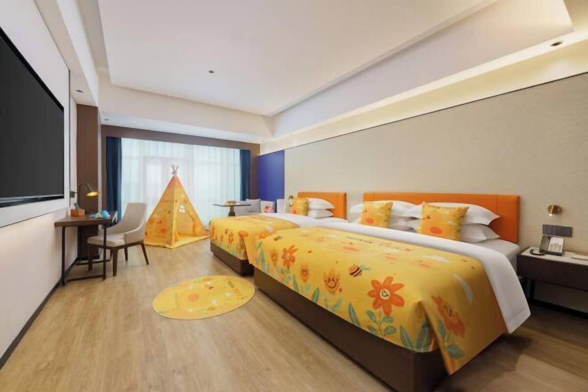 Ein Hotelzimmer mit einem großen Bett, einem Schreibtisch, einem Sessel, einem kleinen Spielzelt und einem Fenster mit Vorhängen.