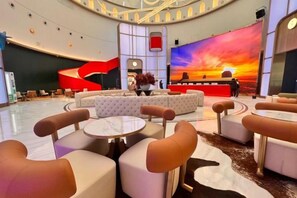 A spacious lobby with a central seating area, a stage with a sunset backdrop, and a modern design. - Vest Holiday Hotel (Urumqi)