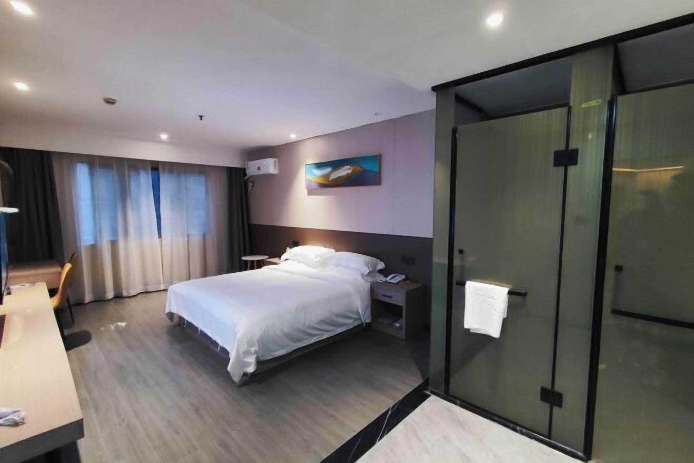 Quarto de hotel moderno com uma cama grande, mesas de cabeceira, uma escrivaninha e um painel de vidro.