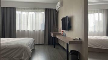 Quarto de hotel com duas camas, uma escrivaninha, televisão e janela com cortinas.