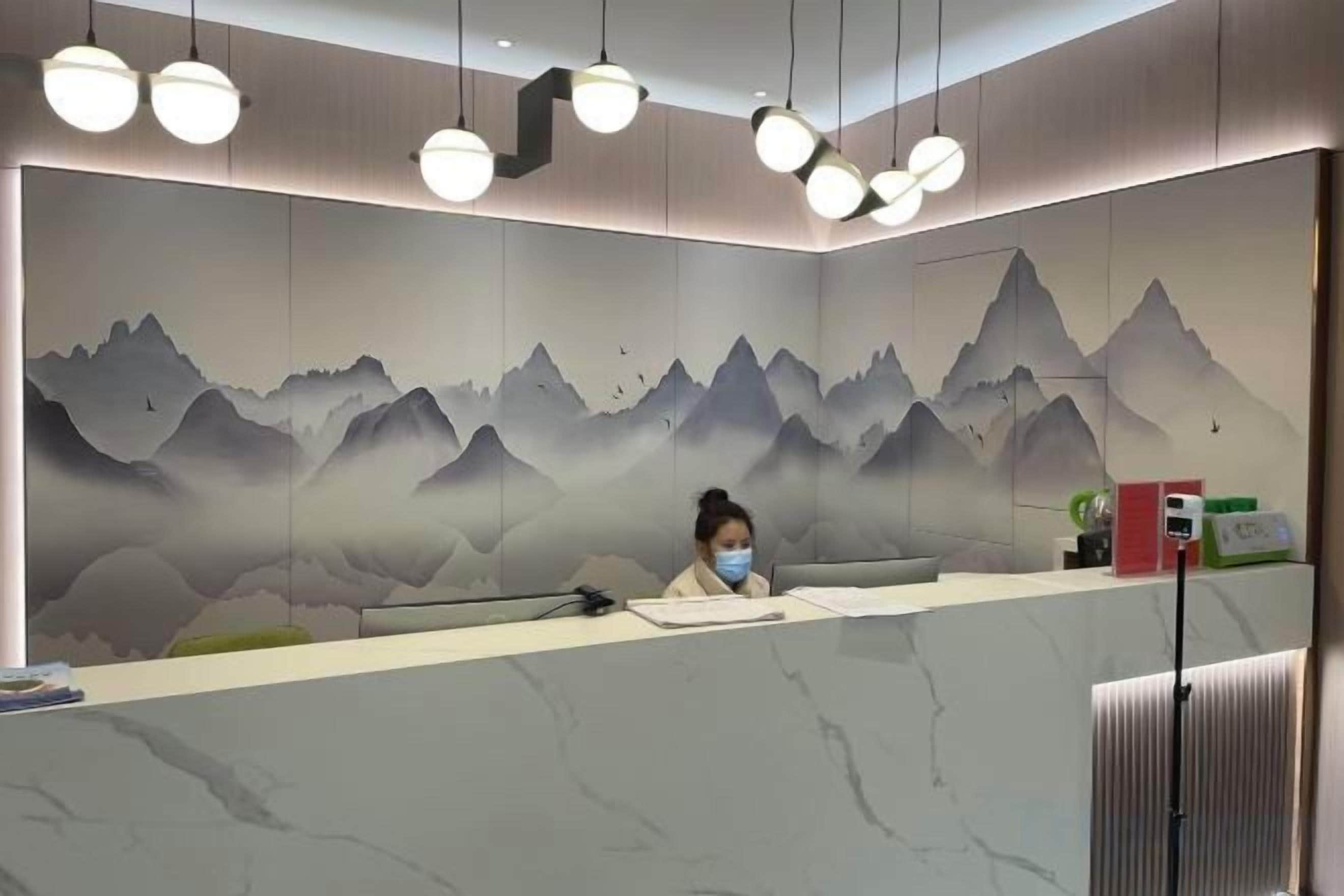 A reception desk with a marble top, a woman seated behind it, and a wall mural of mountains.