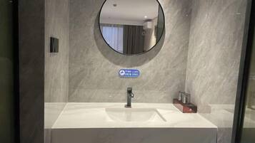 A modern bathroom with a marble sink, a round mirror, and a blue sign above the mirror.