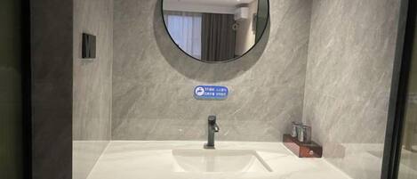 Un baño moderno con un lavabo de mármol, un espejo redondo y una señal azul encima del espejo.