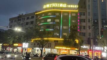 A multi-story building with illuminated signage, a street in front, and vehicles.