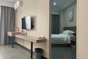 A hotel room with a bed, a desk with a television, a trash bin, and a wall-mounted air conditioning unit. - Taizhou 1981 Hotel (Sanmen Shangyang Road Branch) (Sanmen)