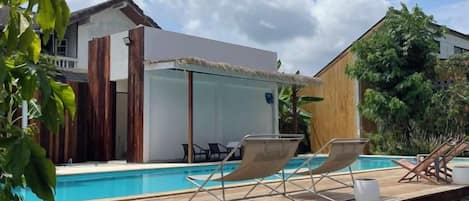 A modern pool area with lounge chairs, a glass-enclosed structure, and a wooden deck.