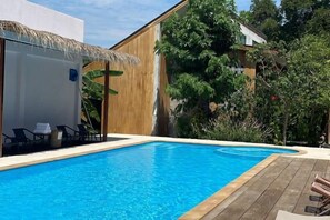 A swimming pool with a wooden deck, a covered seating area, and a building with a white exterior and wooden accents. - Likita Resort (Rayong City)