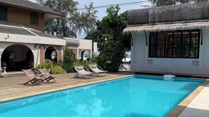 A swimming pool with lounge chairs, a thatched-roof structure, and a building with arched windows. - Likita Resort (Rayong City)