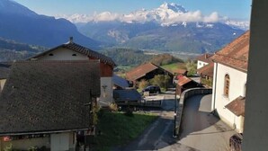 Ein Bergdorf mit traditionellen Häusern, einer engen Gasse und Blick auf verschneite Berggipfel in der Ferne.