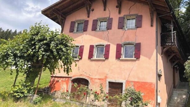 Ein zweistöckiges Gebäude mit einem geneigten Dach, zahlreichen Fenstern mit Fensterläden und einem kleinen Balkon.