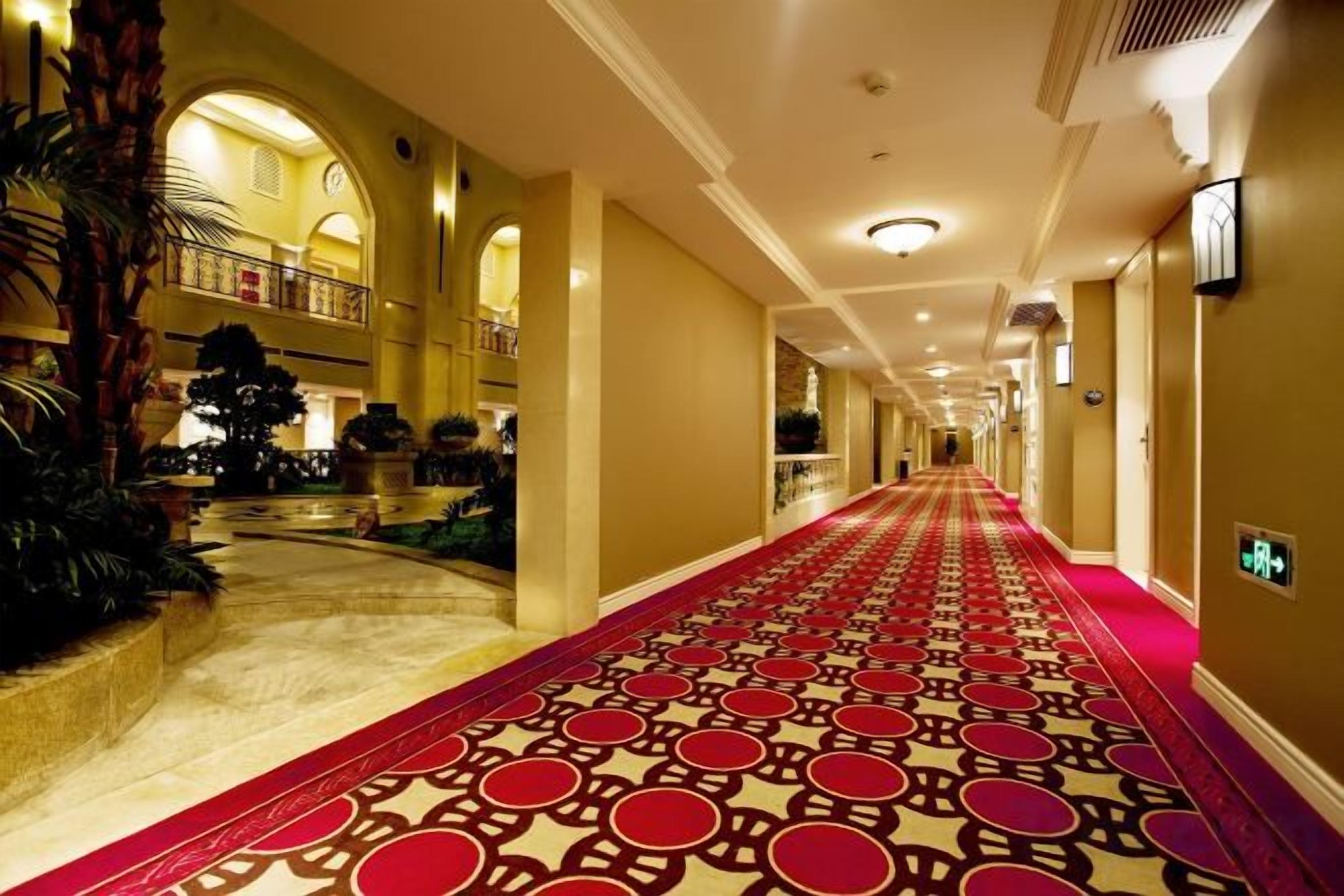 A hotel corridor with a patterned carpet, arched ceilings, and a view of the lobby area.
