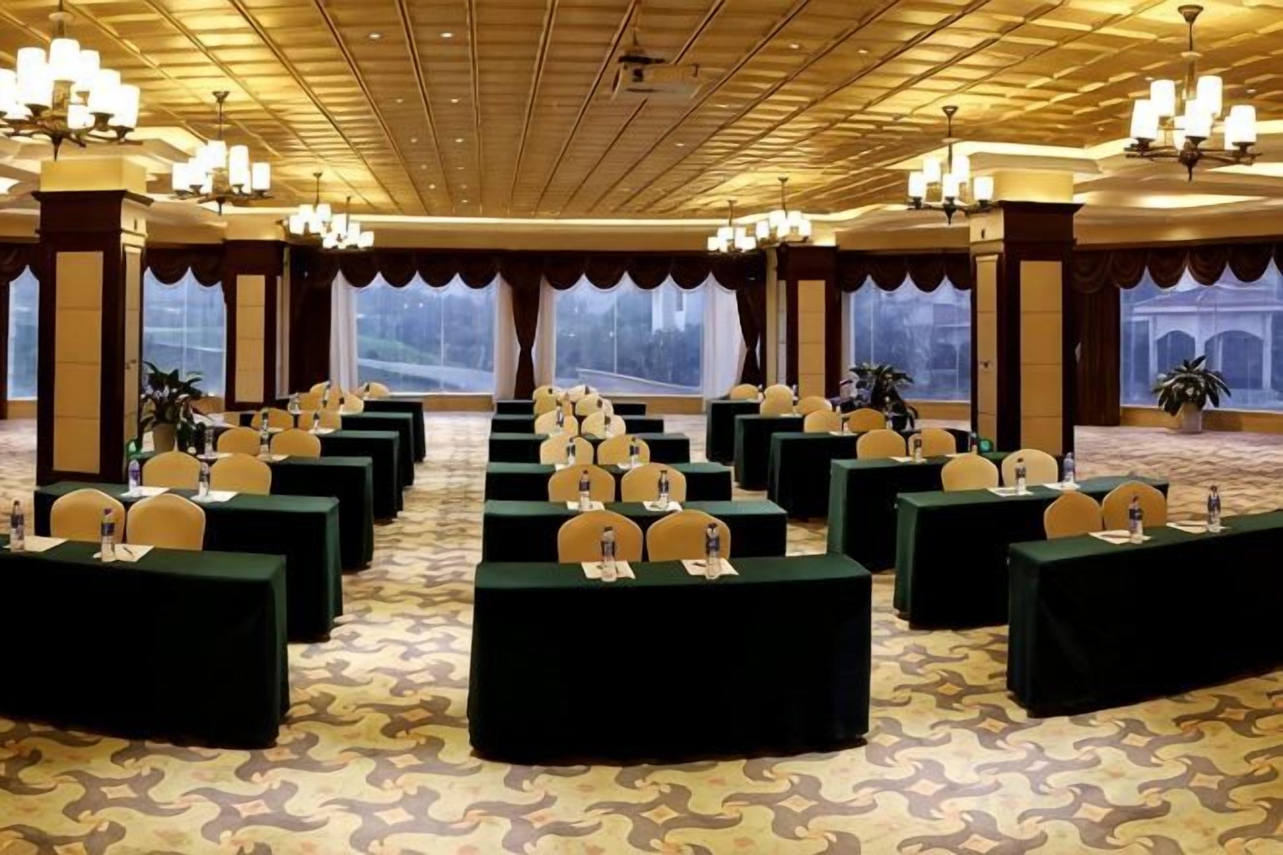 A conference room with multiple tables and chairs, large windows, and chandeliers.