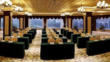 A conference room with multiple tables and chairs, large windows, and chandeliers.