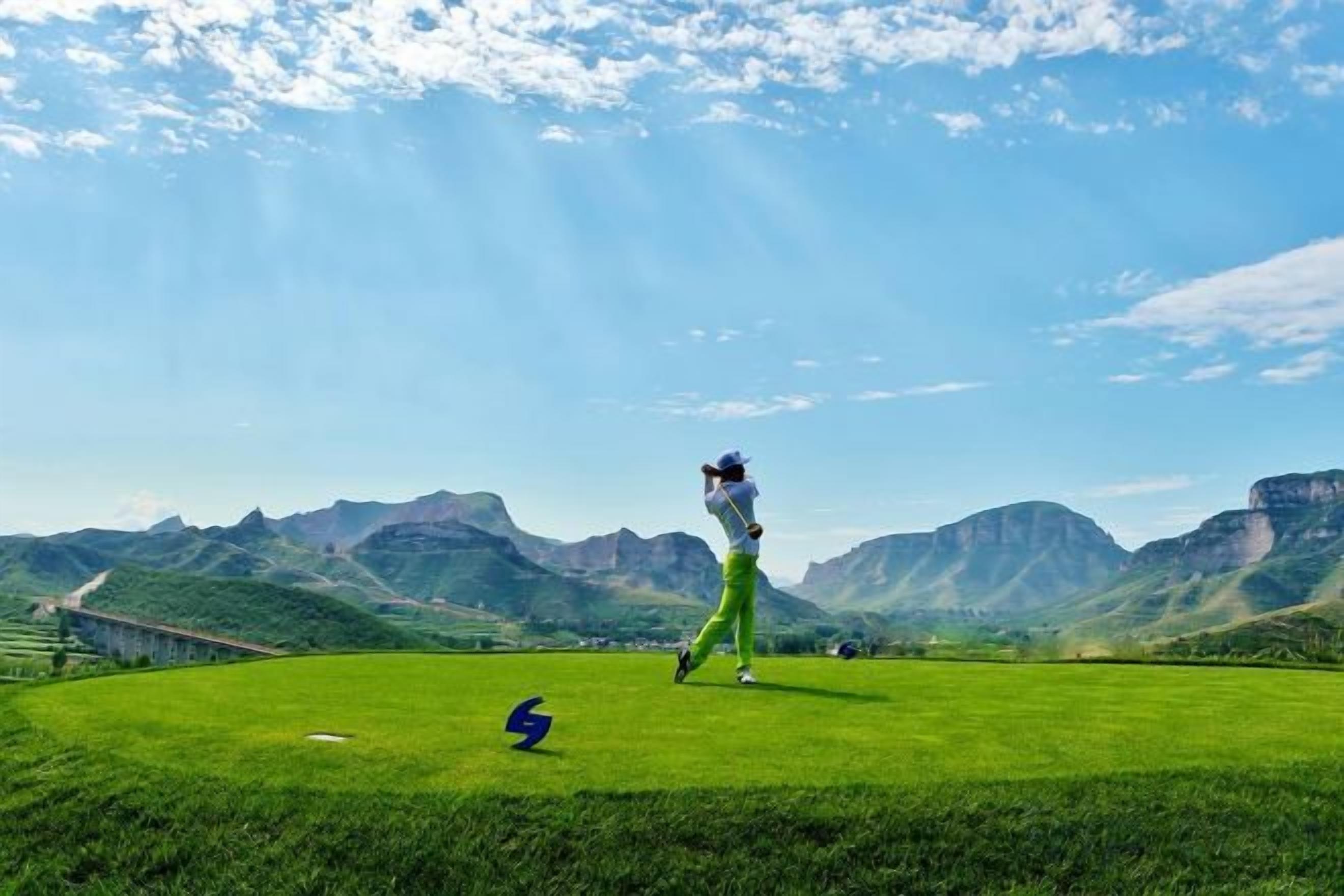 A golf course with a clear sky, distant mountains, and a single golfer in motion.