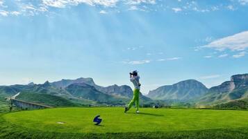 A golf course with a clear sky, distant mountains, and a single golfer in motion.
